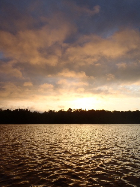 Behind trees and the river, the sun emerges for another day. NPS photo.