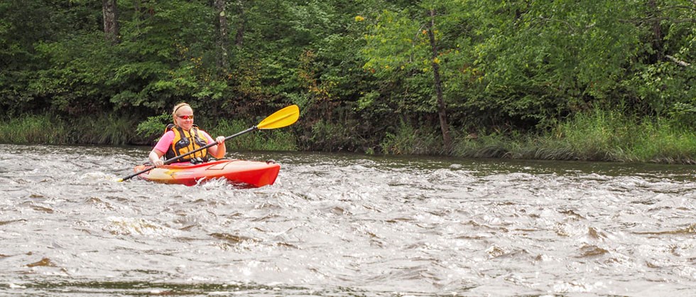 A woman paddles a kayak in moving water. A woman paddles a kayak in moving water.