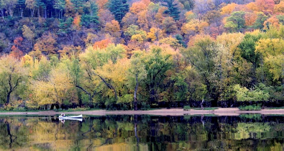 A canoer glides past autumn color reflected in a river.