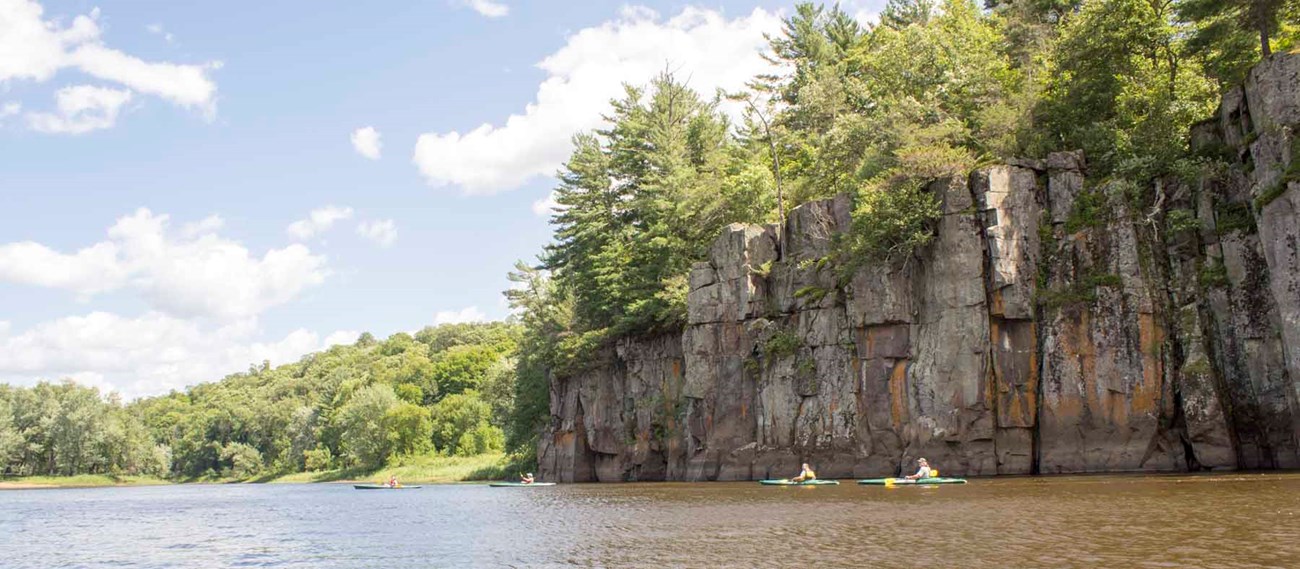 Kayakers paddle past tall basalt cliffs.