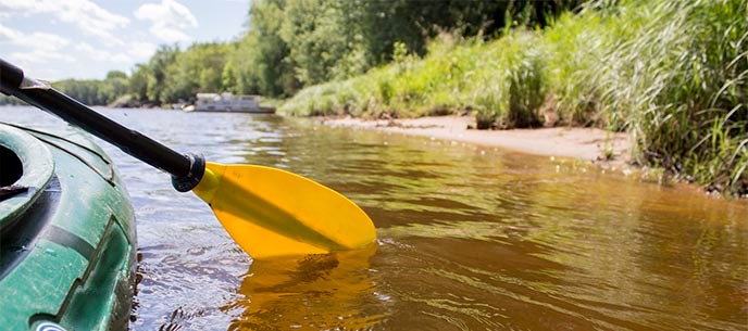 A yellow paddle dips into a river from the side of a kayak.
