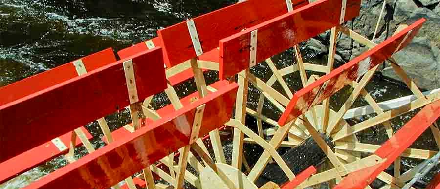 A red paddlewheel turns in water.