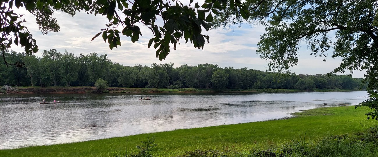 Boaters paddling down the middle of the St. Croix River on a summer's day. Green vegetation outlines the river's edges.