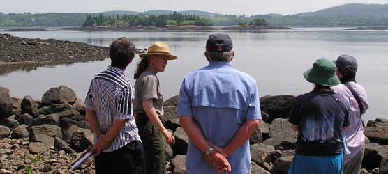 Park employee talks with four visitors with a view of the island in the background.