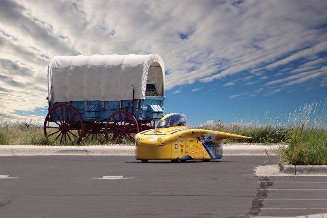 A solar car next to a covered wagon.