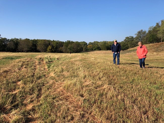 People walk in a grassy field next to a swale in the landscape.