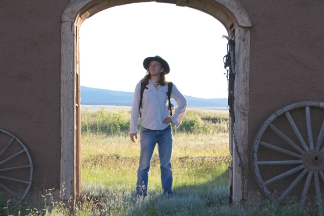 Student Conservation Association intern Noah stands in a doorway of a historic site surrounded by prairie.
