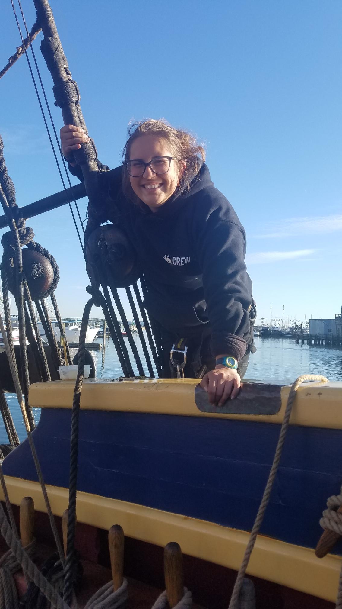 Sara tuning the rig of the Lady Washington Woman with arm around block and rigging, leaning on ship's rail