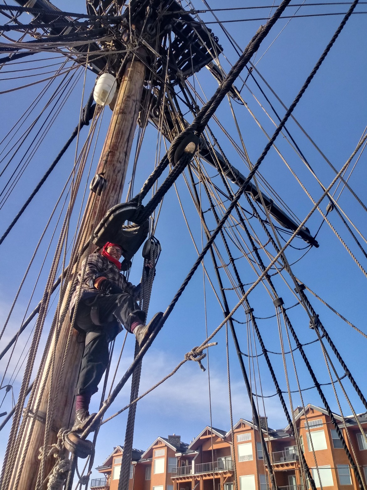 Becca while standing aloft Looking up to a woman standing on the rigging lines (ropes) in front of the ship's mast