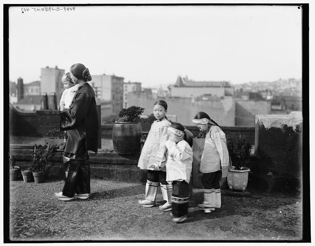 A Chinese or Chinese-American woman and three Chinese or Chinese-American girls walk across a city rooftop. 