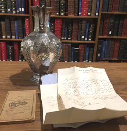 An ornately engraved silver pitcher and old letters.