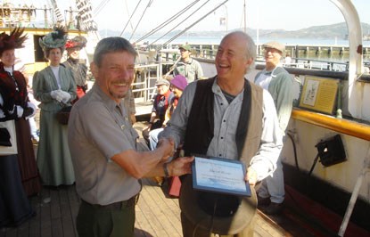 The volunteer coordinator shaking hands with a volunteer and standing on the deck of Balclutha.