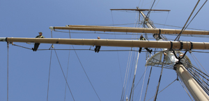 Three park rangers aloft on BALCLUTHA standing on the footrope and holding onto the mainmast yard. Three park rangers aloft on BALCLUTHA standing on the footrope and holding onto the mainmast yard.