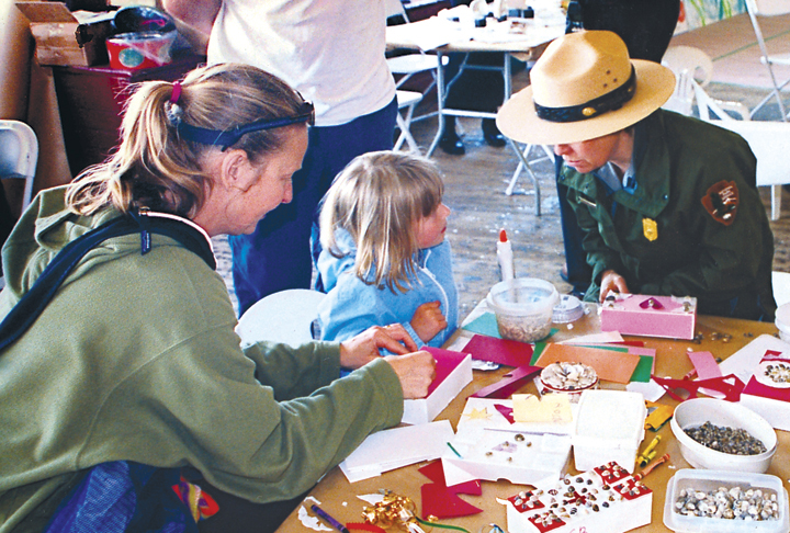 A park ranger at a table with a child doing maritime crafts. A park ranger at a table with a child doing maritime crafts.