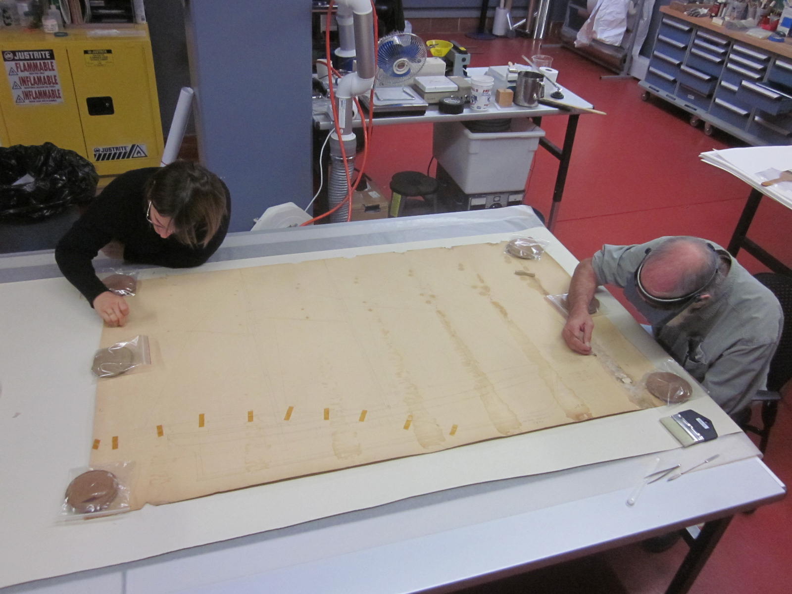 Two conservators at a table cleaning the Bendixsen drawing