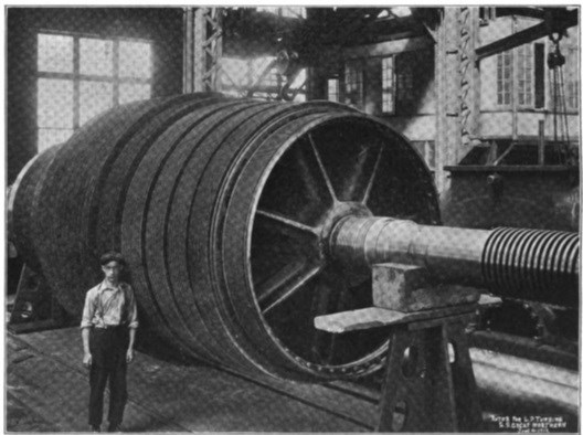 A young man standing next to a giant rotor towering above him.