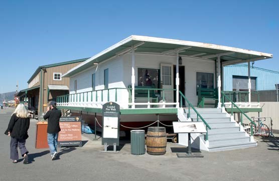 A wooden houseboat painted white with green trim, a front porch, and sitting on dry land.