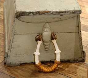 One end of a sailor's sea chest with a rope handle attached to the side.