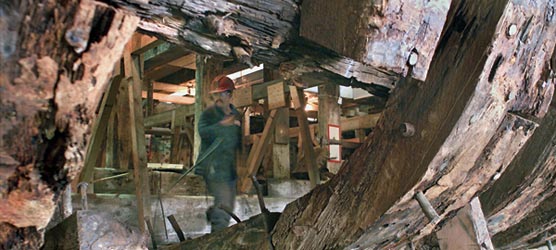 Below decks photo of ship worker looking at ravages of dry rot to Thayer's timbers.