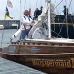 A man standing at the helm of a sailboat.