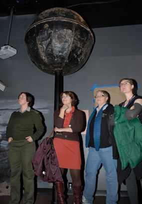 Four people standing near a large cylinder atop a pole.