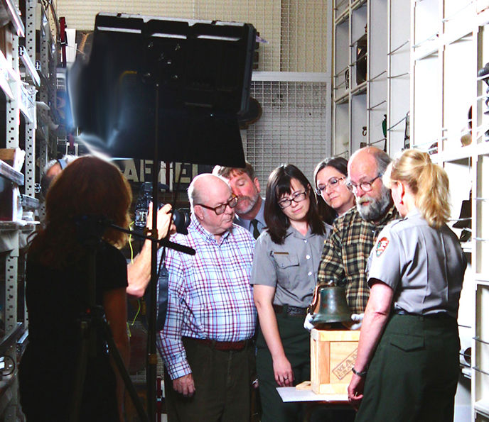 A group of people standing close together and looking with interest at an old bell.