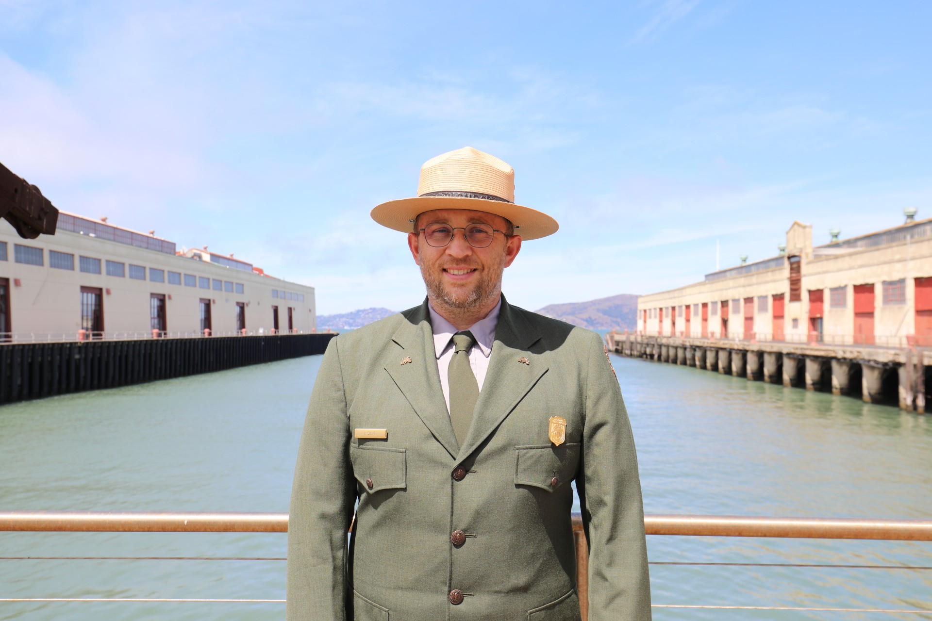 A park ranger in uniform stands in front of buildings in For Mason