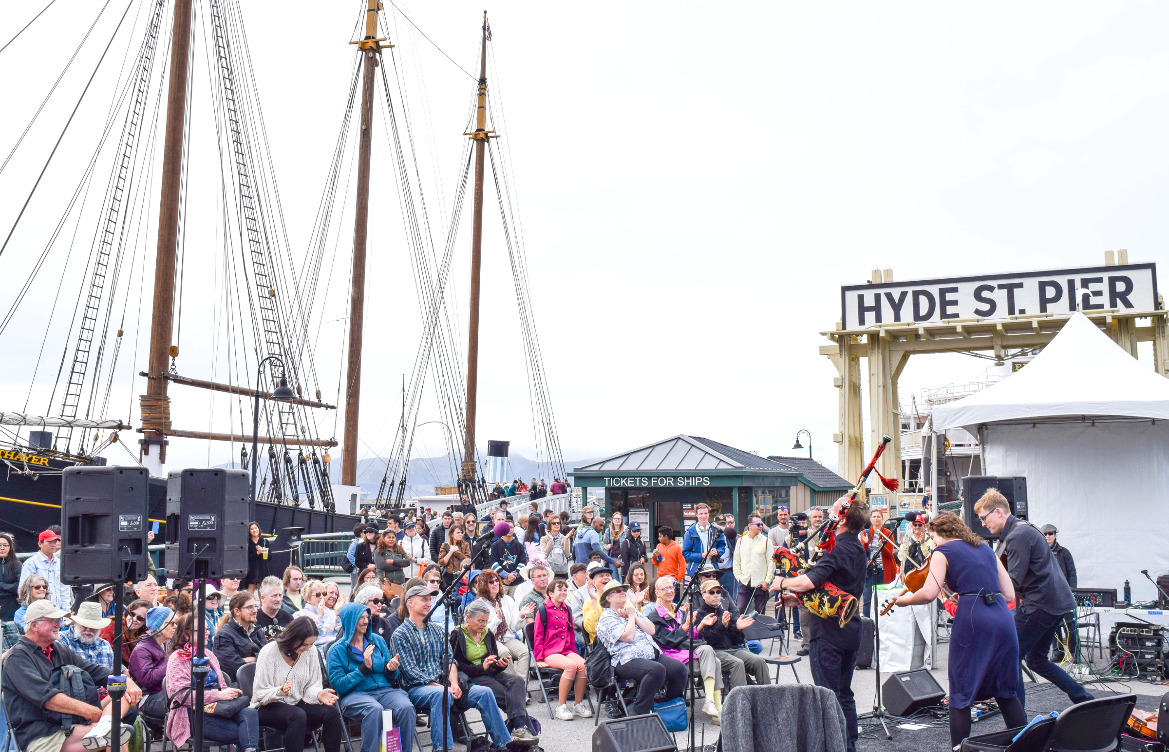 Festival of the Sea Mid-Pier Stage Crowd of people sitting in folding chairs and standing to watch a band perform on a stage near the Eureka ferryboat gangway.
