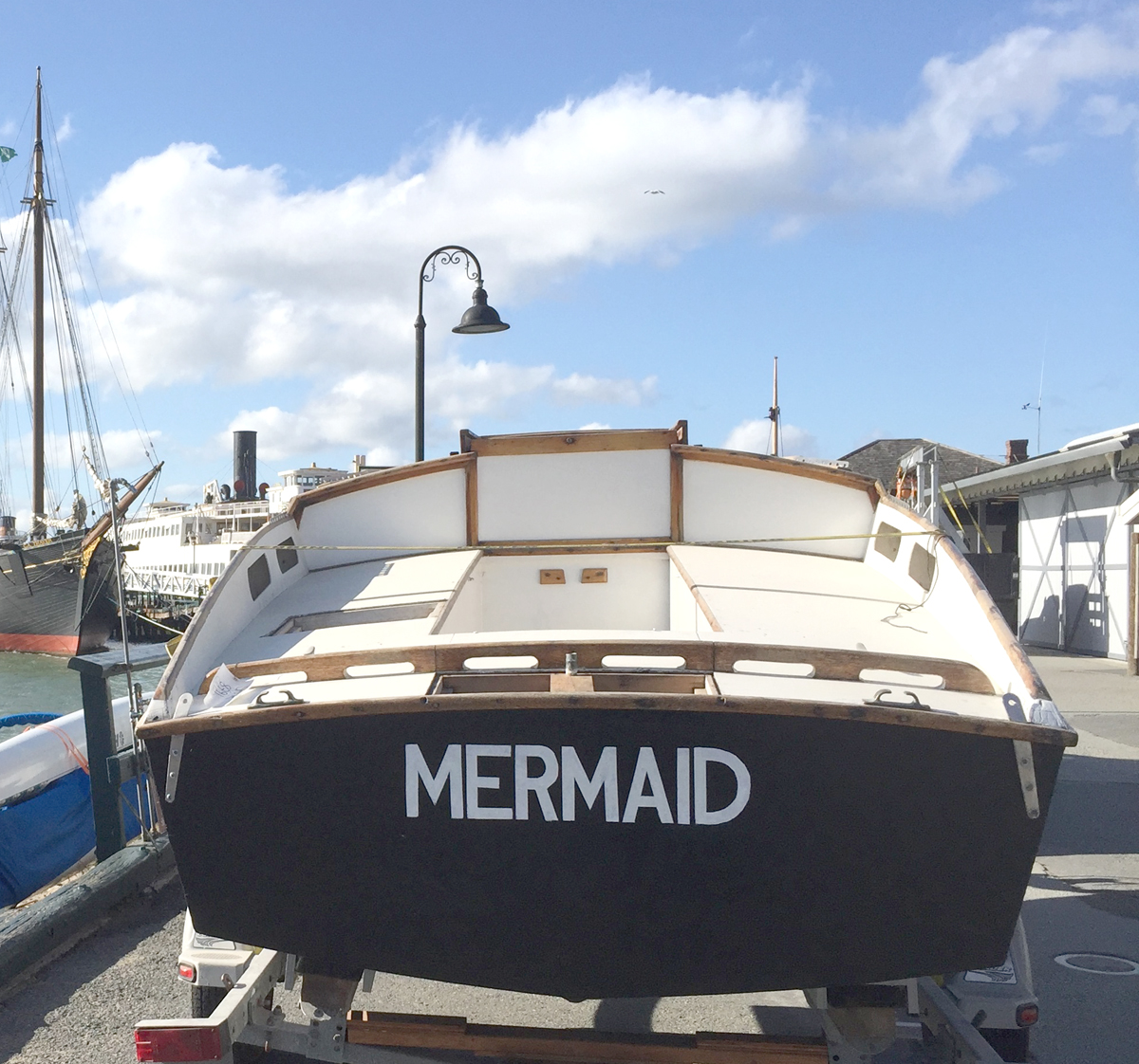 Small boat Mermaid sitting on a trailer at Hyde Street Pier. Viewed from the stern with the name "Mermaid" visible.