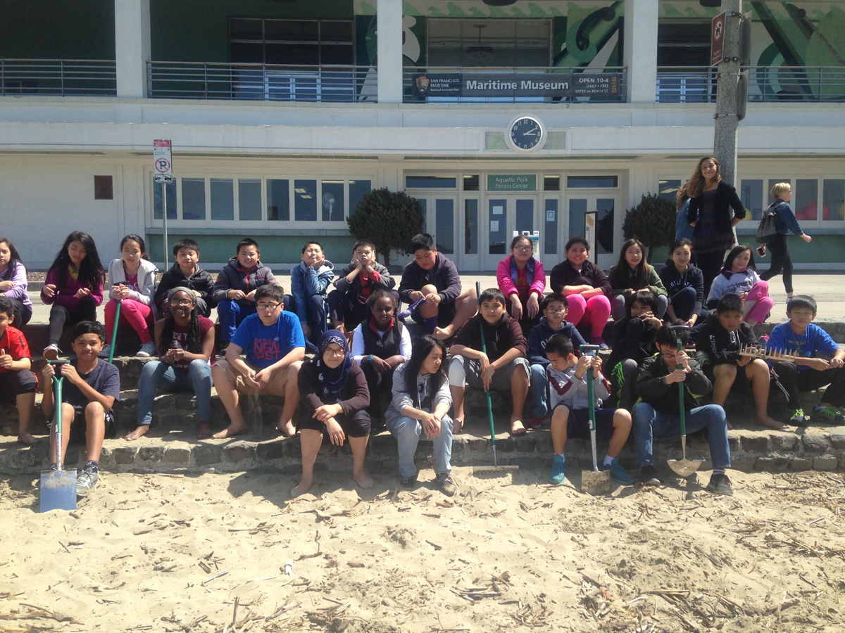 Francisco Middle School Shark Stewards Approximately 30 middle school students, holding shovels and rakes, sitting on stone steps in front of the Maritime Museum