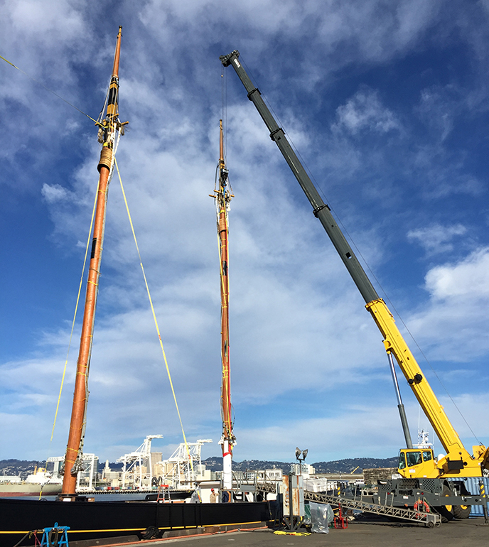 A crane hoisting a 100 foot mast into place on a lumber schooner.