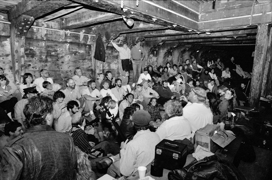 Black and white photo of people sitting in the hold of a wooden ship.