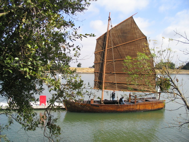 A shrimp junk floating in the water with a dark-brown colored sail raised.