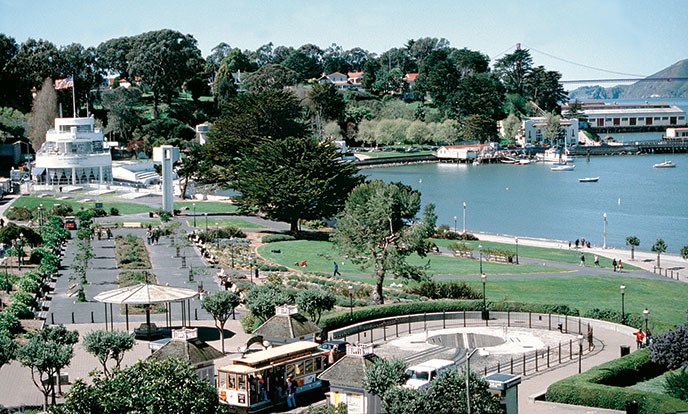 The Aquatic Park Historic District includes gardens, lawns, a cable car turnaround and lagoon. The Maritime Museum building is in the background and the Golden Gate Bridge is visible on the far right.