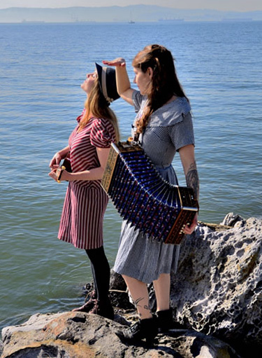 The musical duo Penny Opry: two women standing on a rock at the water's edge.