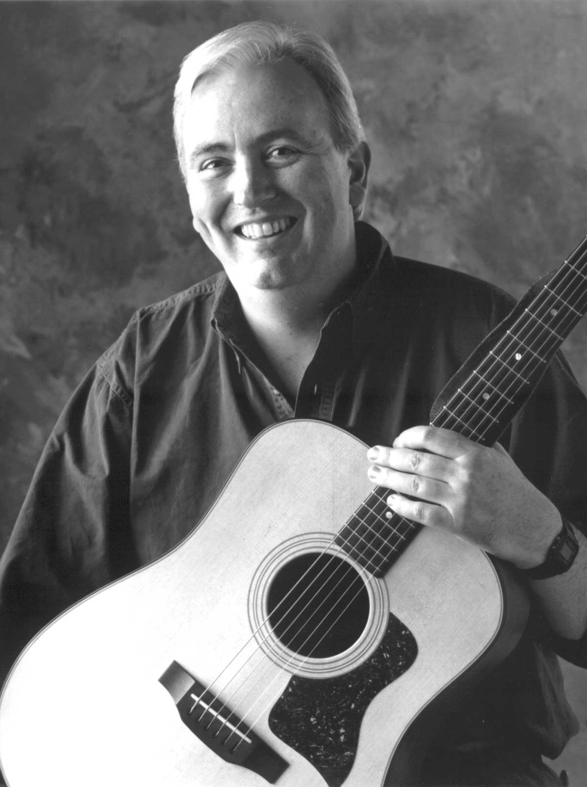 Robbie O'Connell holding a guitar and smiling.