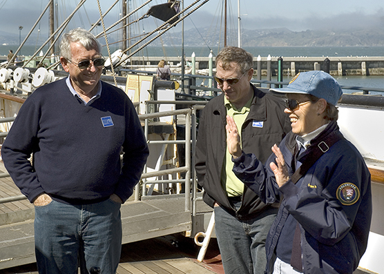 A woman who volunteers at the park speaking with two men aboard the historic sailing ship BALCLUTHA.