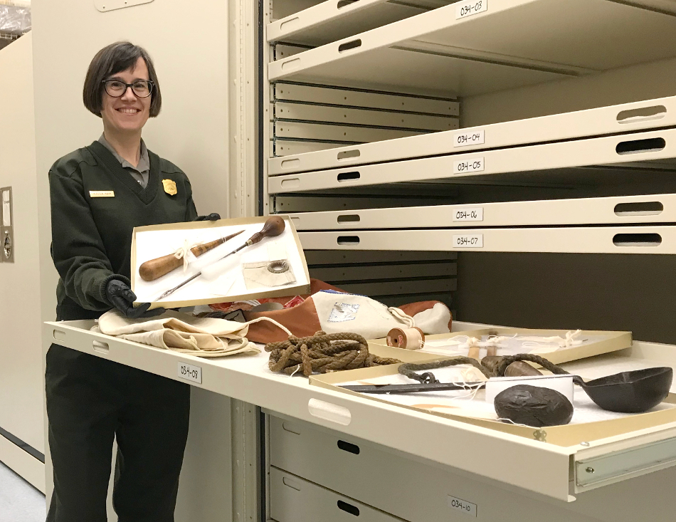 Park Registrar in NPS uniform holding a tray containing various tools for making sails.