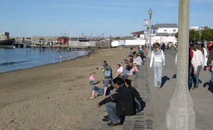 People sitting on a low wall along a sandy beach.
