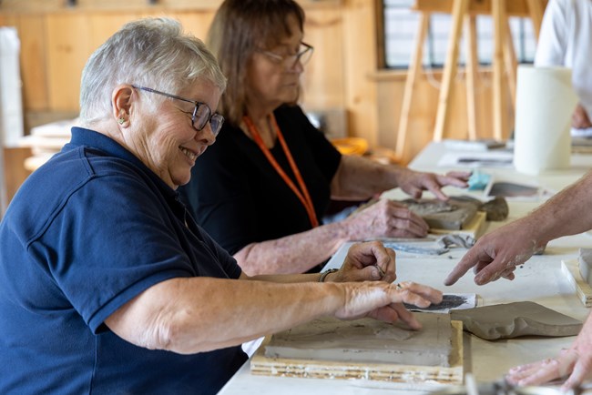 Seated woman smiles as she sculpts flat relief