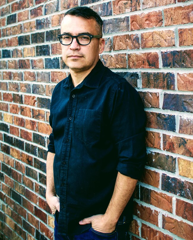sculptor poses in front of brick wall