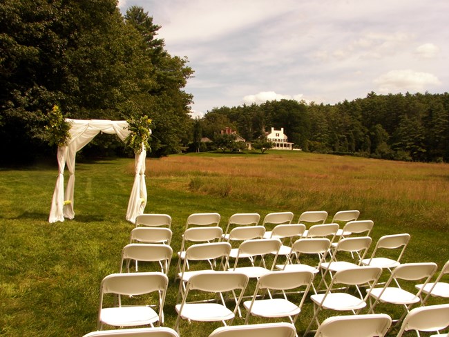 white folding chairs and arch with white curtains in field with Aspet home far in the distance