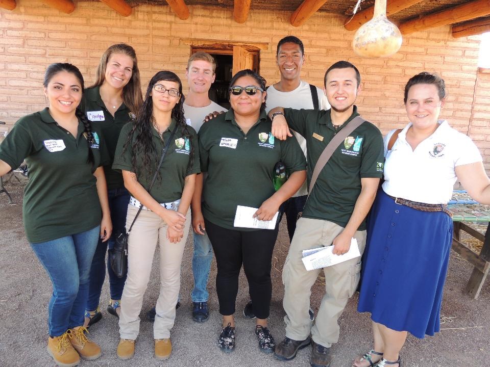 Group of 8 young adults, most in matchin green polo shirts with NPS arrowhead and Friends of Saguaro National Park logo