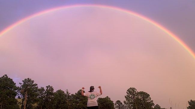 Crew member poses in front of a rainbow