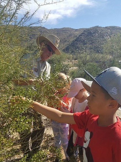 Volunteer Ranger observes plant with students. Volunteer Ranger observes plant with students.