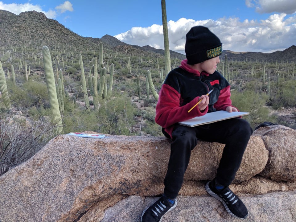 youth with paintbrush sitting on rock in front of desert landscape