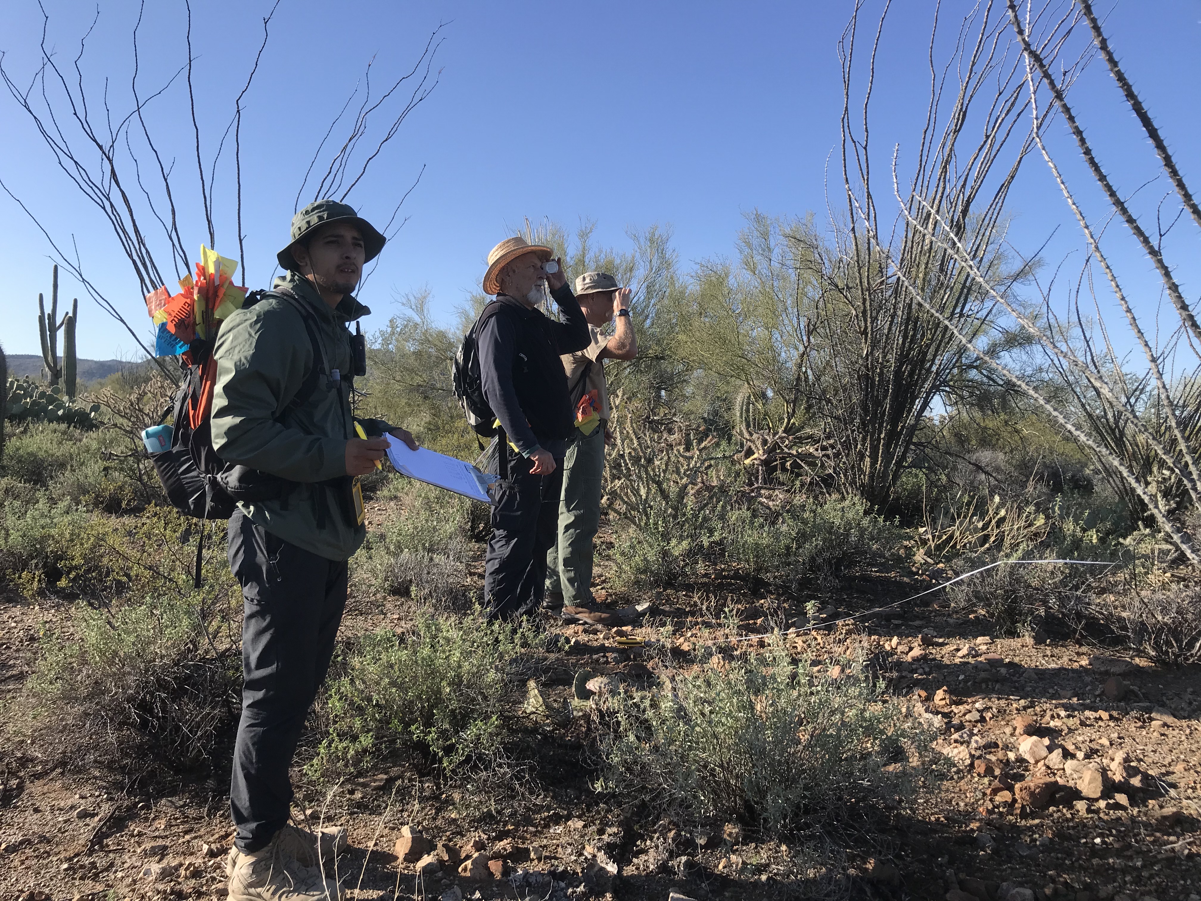 Two volunteers using a clinometer. To their right is a park staff holding a clipboard.