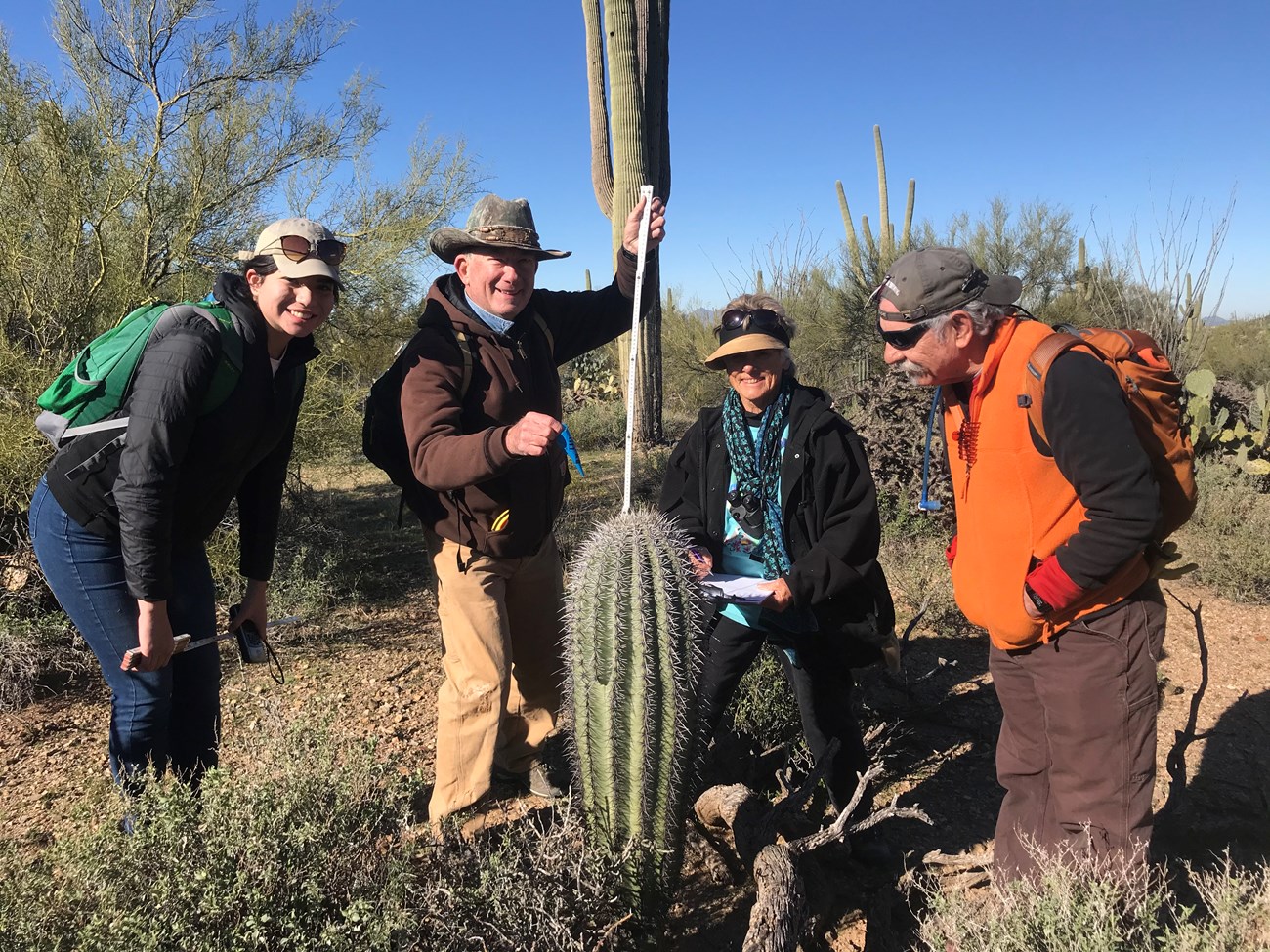 Volunteers smiling for a photo. In front of them is a short saguaro.