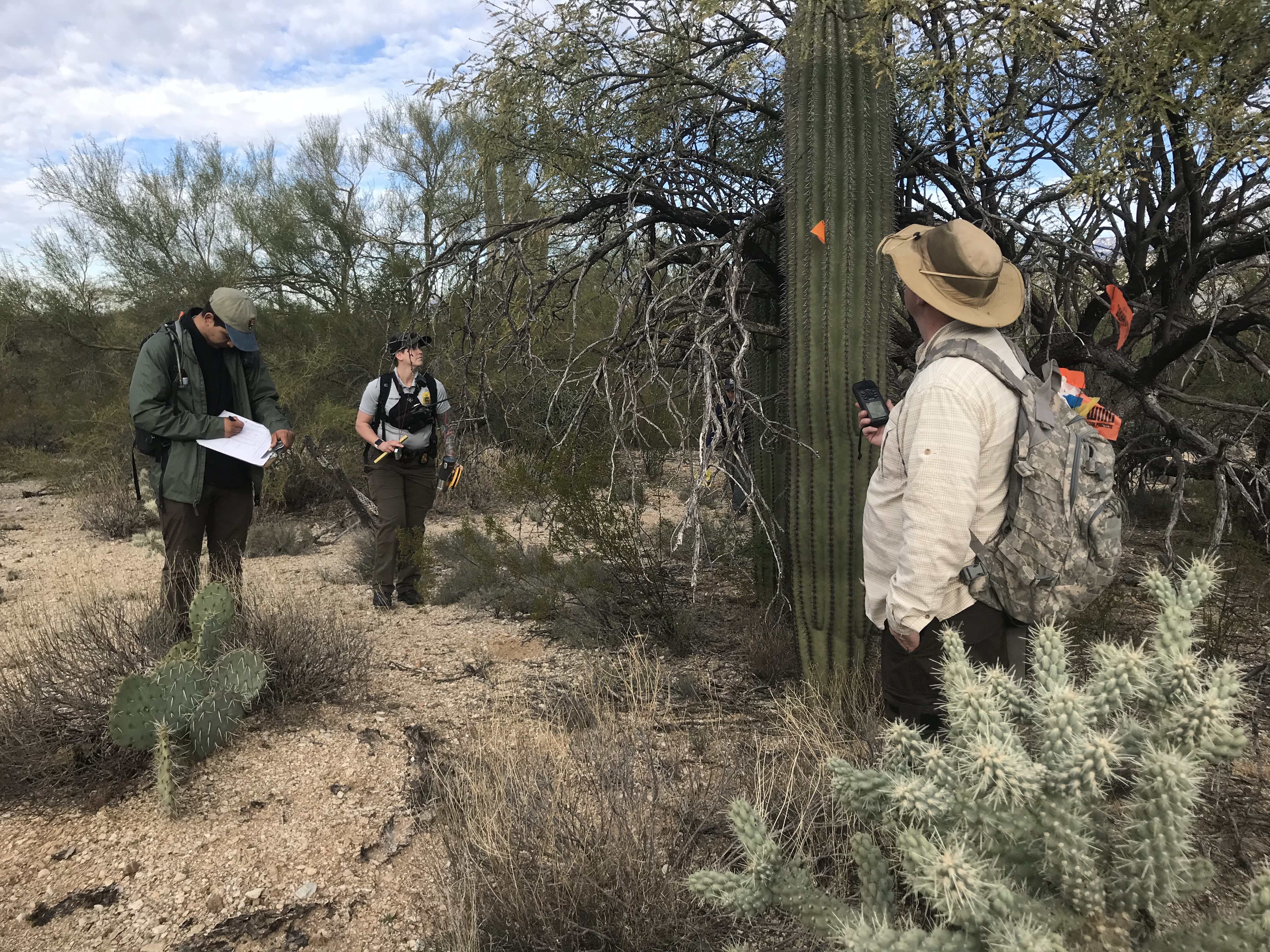 A man holding a gps device while another man is writing down data.