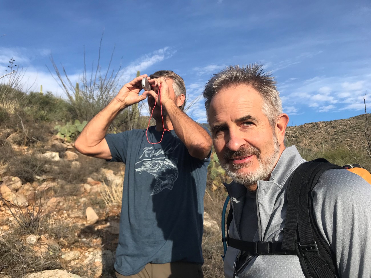 Close up shot of two men, one of whom is using a clinometer to measure the height of a saguaro